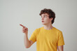 © BetterPhoto - Young man in a yellow shirt pointing with a surprised expression, looking to the side against a plain background.