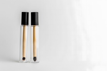 Two makeup brushes are in clear bottles. The two clear bottles, each with a black lid, contain brushes. Minimalist makeup tools.