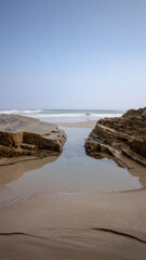 Solitary paradisiacal photograph of a beach between two rocks with clear sky and waves. Concept: Travel, nature, beach, travelling, trips.