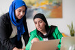 © Studio Marmellata - Two women in hijabs collaborate while looking at a laptop screen together in a modern office. Their engaged expressions show a productive and focused work atmosphere.