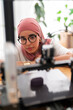 © Studio Marmellata - A woman in a dark red hijab closely adjusts the settings of a 3D printer, demonstrating precision and expertise in handling advanced technology and equipment.