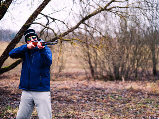 A man in a blue jacket is holding a shotgun. The image has a mood of excitement and anticipation, as the man is preparing to shoot a target. Sport and hobby concept. Male with a rifle.