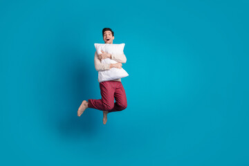 Poster - Full body photo of attractive young man jump hugging pillow dressed pajama sleepover good night isolated on blue color background