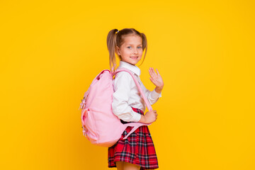 Portrait of little schoolkid bag arm wave hi wear uniform isolated on yellow color background