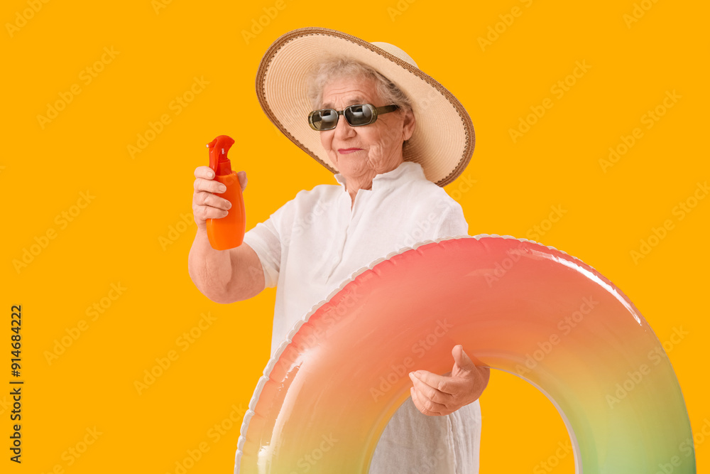 Senior woman with sunscreen cream and inflatable ring on orange background