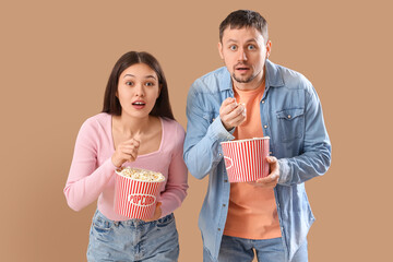 Canvas Print - Young couple watching movie with popcorn on beige background