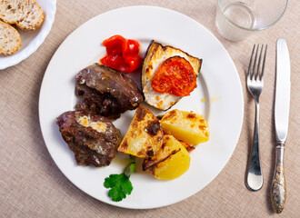 Wall Mural - Delicious grilled pork cheeks served on rustic plate with side of roasted potatoes, tomato, eggplant and pepper for dinner. Traditional Spanish dish