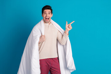 Sticker - Photo of handsome young guy wrapped duvet point empty space dressed sleepwear sleepover good morning isolated on blue color background