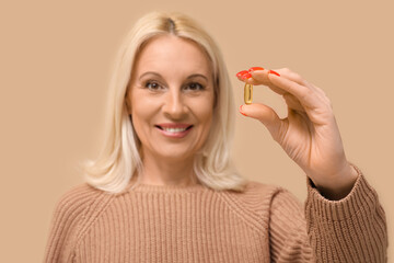 Poster - Mature woman with fish oil pill on beige background