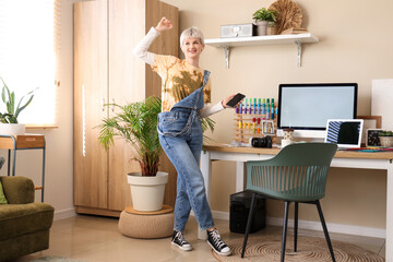 Sticker - Young woman holding mobile phone near workplace with modern computer in light office