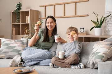 Poster - Little boy with his mother holding glasses of milk and cookies and sitting on sofa in living room