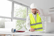 © Pixel-Shot - Male contractor with house plan talking by mobile phone in room
