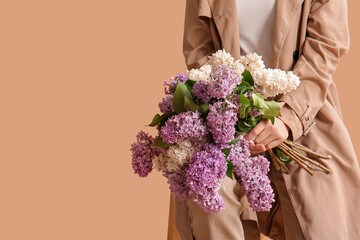 Wall Mural - Beautiful young woman with bouquet of lilac flowers sitting on chair against beige background, closeup