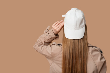 Wall Mural - Young woman in stylish white cap on brown background, back view