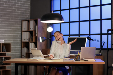 Sticker - Young woman sitting at workplace and talking with phone in office