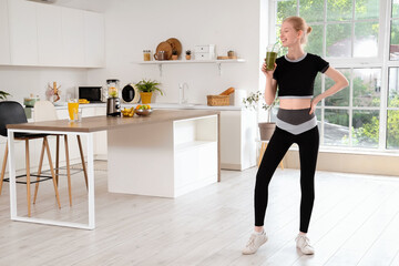 Wall Mural - Happy sporty young woman with healthy smoothie in kitchen