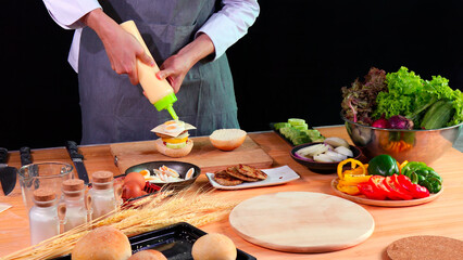 Young Chef stack meat and squeezing potato sauce onto layered burgers with fresh ingredients on kitchen counter