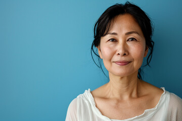 A smiling Asian woman with dark hair and a white shirt poses against a blue background. Her expression is friendly and confident.