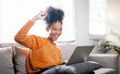© NAMPIX - Excited black woman feel euphoric or happy reading good news online, sits on couch at home