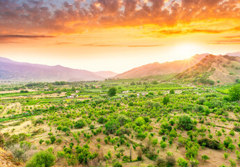 Wall Mural - sunset valley landscape with green trees and gardens among beautiful mountains with colorful cloudy sky on background