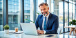© Adisorn - Confident middle-aged businessman sits at desk, using laptop, exuding happiness and professionalism, with a hint of distraction, in a modern office setting with ample copy space.