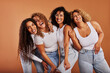 © Flamingo Images - Diverse women in jeans and white tops laughing together on an orange background