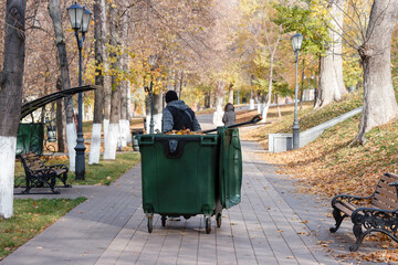 a man is pushing a green trash can down a sidewalk