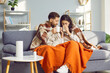 © Studio Romantic - Young couple wrapped in blankets sitting on sofa at home. Happy lovers couple sitting together holding mugs of hot drink in hands in cold winter weather. Husband and wife warming themselves at home