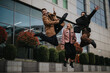 © qunica.com - Three young professionals in smart casual wear are leaping joyfully in the air outside a contemporary office setting, displaying a sense of freedom and happiness.