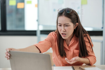 A woman in an orange shirt is looking at a laptop computer