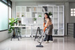 © Natee Meepian - Professional Maid Cleaning Modern Office Space with Vacuum Cleaner in Bright, Organized Environment