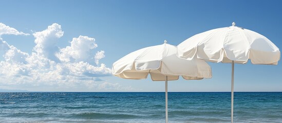 Aufkleber - Close up of two closed white canvas beach umbrellas set against a backdrop of the sea and a blue sky with clouds. with copy space image. Place for adding text or design