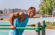 © Iona - man performs tricep dips on outdoor bars, smiling and enjoying the exercise on a sunny day in an urban park