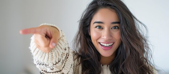 Hispanic woman with long hair dressed in a casual winter sweater is smiling and looking amazed at the camera while gesturing with her hand and pointing with her finger. with copy space image