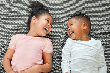 Wall Mural - Top view, siblings and laughing on bed together, happiness and funny conversation for bonding in home. Above, children and bedroom for silly humor in communication, brother and sister for family love