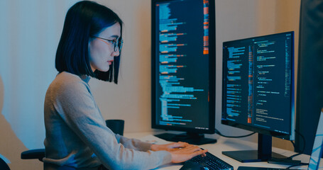 Young Asia female freelance eyeglasses typing write prompt AI bot IT app smart program nomad, video game, terminal with coding language, designer, big data center on desktop computer in night office.