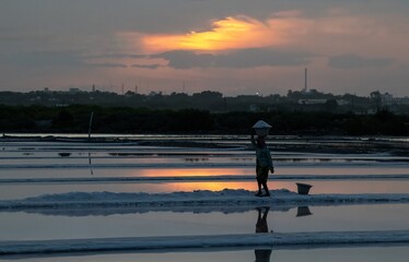 Wall Mural - Silhouette of a woman working at a salt pan in Tuticorin India at sunset.  The woman is carrying salt on her head and walking