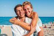 © Jose Calsina - Close up portrait of a young Caucasian tourist couple hugging and looking at the camera on the beach while enjoying their summer vacation on the coast. Two people smiling together at a beach bar