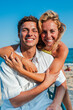 © Jose Calsina - Vertical portrait of a young Caucasian tourist couple hugging and looking at the camera on the beach while enjoying their summer vacation on the coast. Two people smiling together at a beach bar