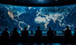 © panumas - A group of people are sitting in front of a large screen that shows a map of the world