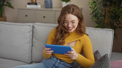 Sticker - A young, beautiful, blonde caucasian woman in a yellow sweater is sitting in her living room, using a digital tablet and phone, within a cozy home setting.