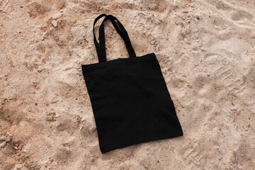 Black cotton or mesh bag on beach sand background. Zero waste, no plastic, eco friendly shopping, recycling concept. Blank mockup shopper with place for artwork or text. Flat lay, copy space