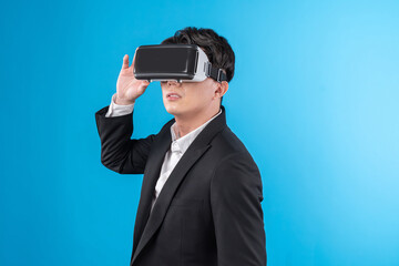 Smiling Asian businessman looking thorough VR connecting to business world report in futuristic metaverse, analyzing innovation technology ads in virtual reality isolated blue copyspace. Contrivance.