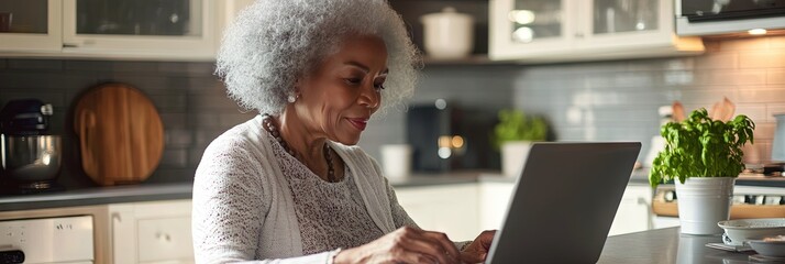 Wall Mural - older african american woman working on laptop, in kitchen, copy space 