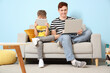 © Pixel-Shot - Little boy with his father using gadgets on sofa at home