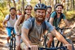 © Dipsky - A group of friends riding bicycles in the lush green woods. A bearded man leads the way, smiling at the camera. All riders are wearing helmets and enjoying the outdoor adventure together.