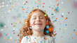 © NooPaew - Happy child girl celebrating with colorful confetti, bright smile on her face against a white background