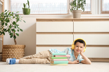 Poster - Cute little Asian boy in headphones listening to audiobook with books while lying on carpet in living room