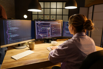 Canvas Print - Female programmer working with computer in office at night, back view