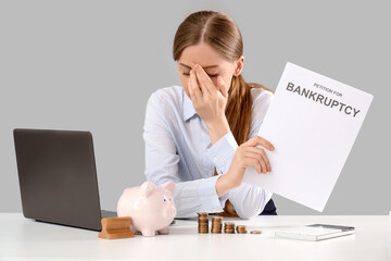 Poster - Stressed businesswoman with petition to file for bankruptcy at table on light background